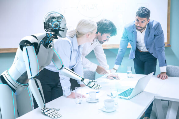 Three humans and an android robot lean over a desk with a laptop and have a discussion.