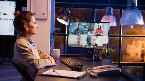 A woman sits at a computer desk and speaks with four people on her computer screen in a video chat.