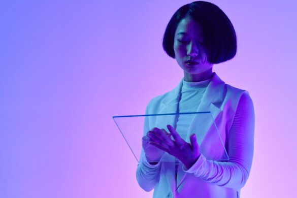 A woman looks at a futuristic, transparent data tablet that she holds in her hands as she stands in front of purple and pink background.