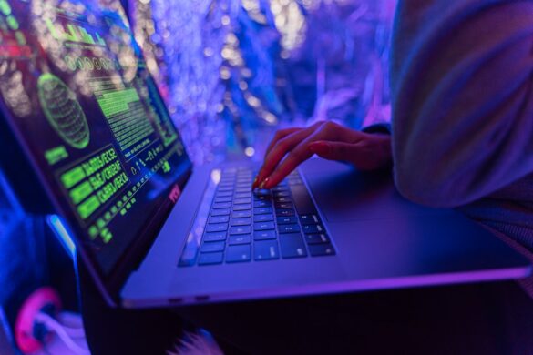 A female hand typing on a laptop with blurred lights in the background.