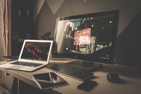 A desk with a laptop, large screen, tablet, phone and keyboard resting on it.